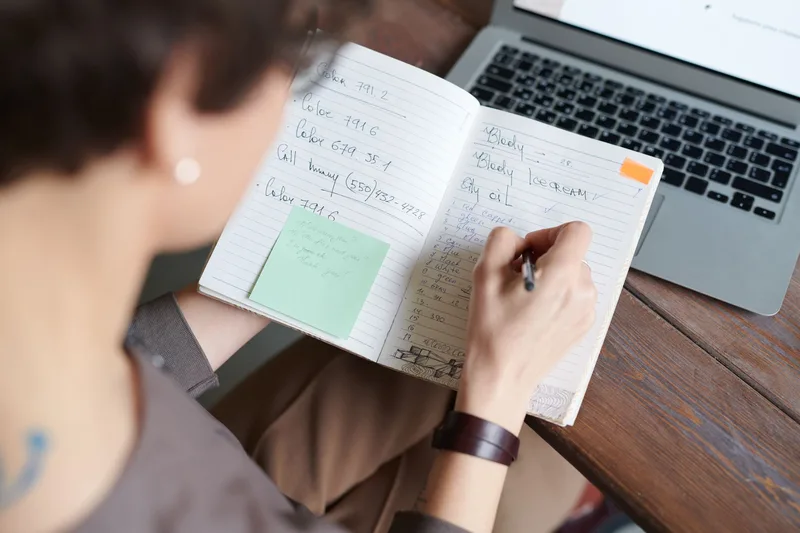 Marketer taking handwritten notes next to a laptop while researching creative ideas