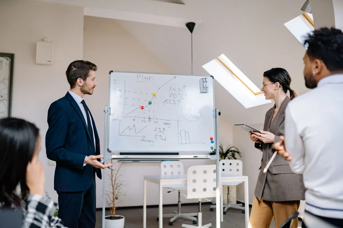 Colleague presenting a plan chart on a whiteboard to a team in an office