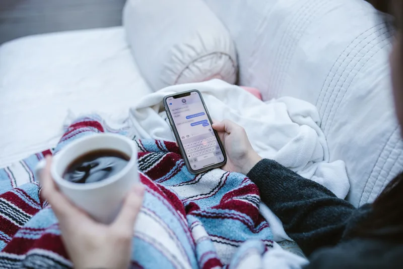Person reading a message thread on a smartphone while holding a cup of coffee