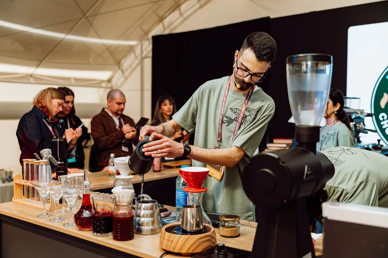 Barista running a pour-over coffee demonstration at a live event while attendees watch