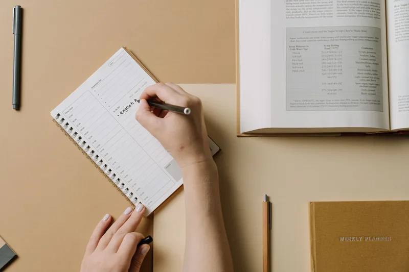 Hands writing in a weekly planner on a desk