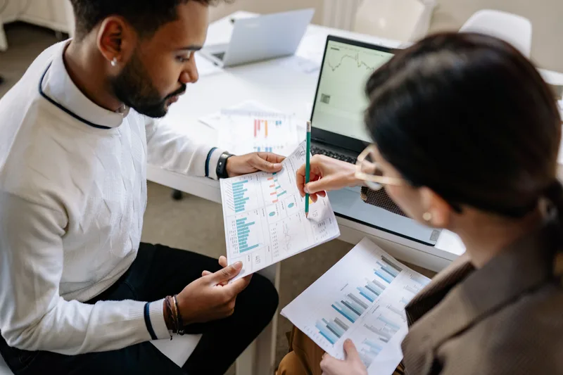 two analysts reviewing printed bar charts and a laptop showing a trend line, comparing collection page performance before and after a change