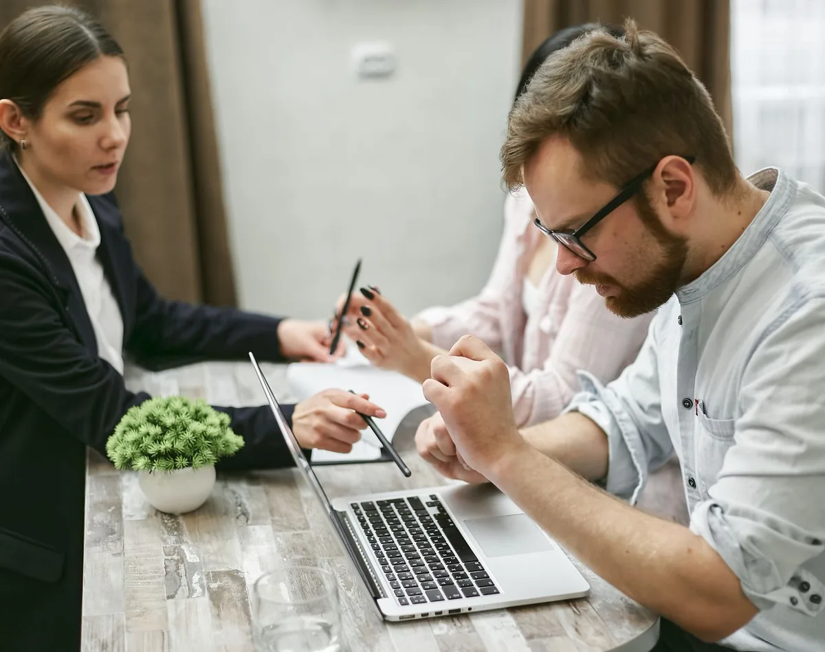 Three colleagues gathered around a laptop at a wooden table, discussing a decision