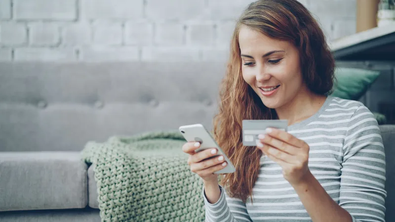 Shopper on a sofa holding a smartphone and a credit card, about to complete an online purchase