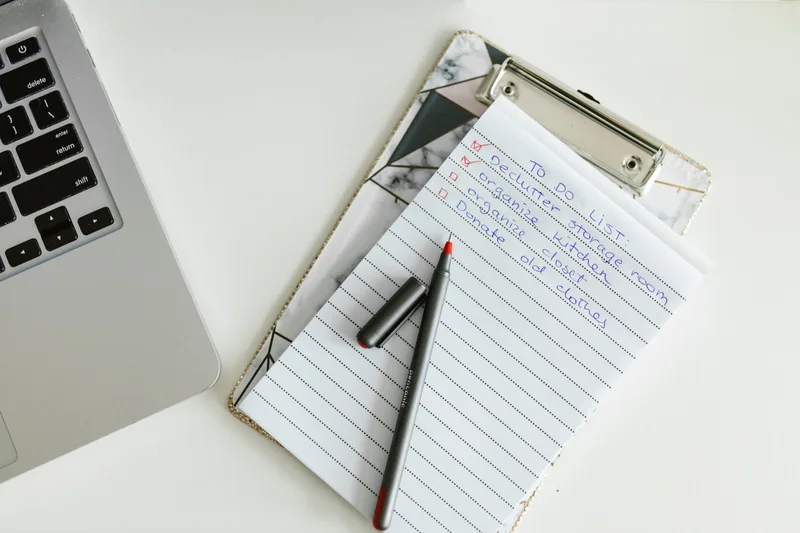 Handwritten checklist on a clipboard beside a laptop, with a pen resting on top
