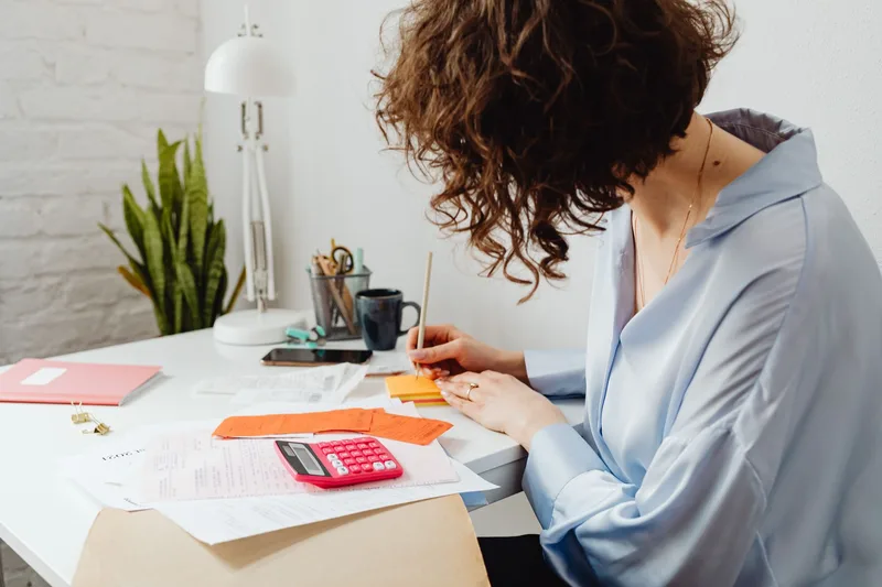 Person using a calculator while writing notes at a desk, cross-checking totals
